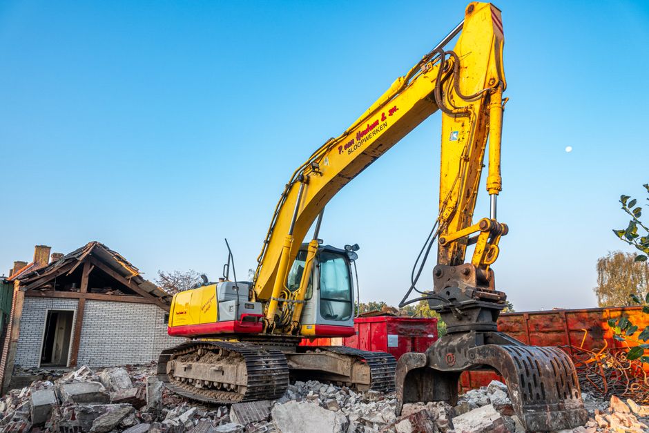 A large yellow excavator working amidst rubble at a construction site under a clear blue sky.