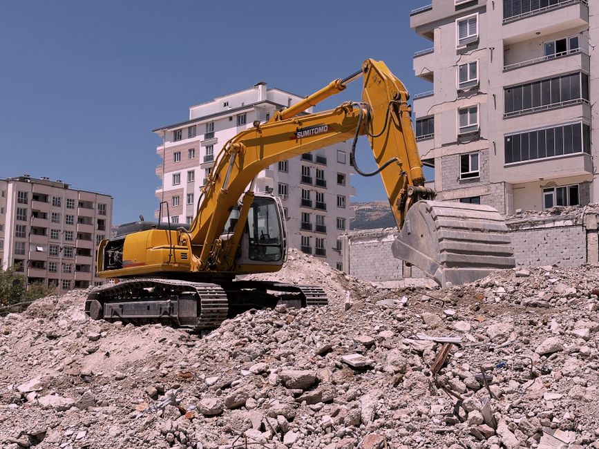 Yellow excavator working among rubble at a construction site.